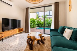 Una sala de estar moderna con un televisor de pantalla plana, un mueble de entretenimiento de madera y un sofá verde con una mesa de centro trenzada.