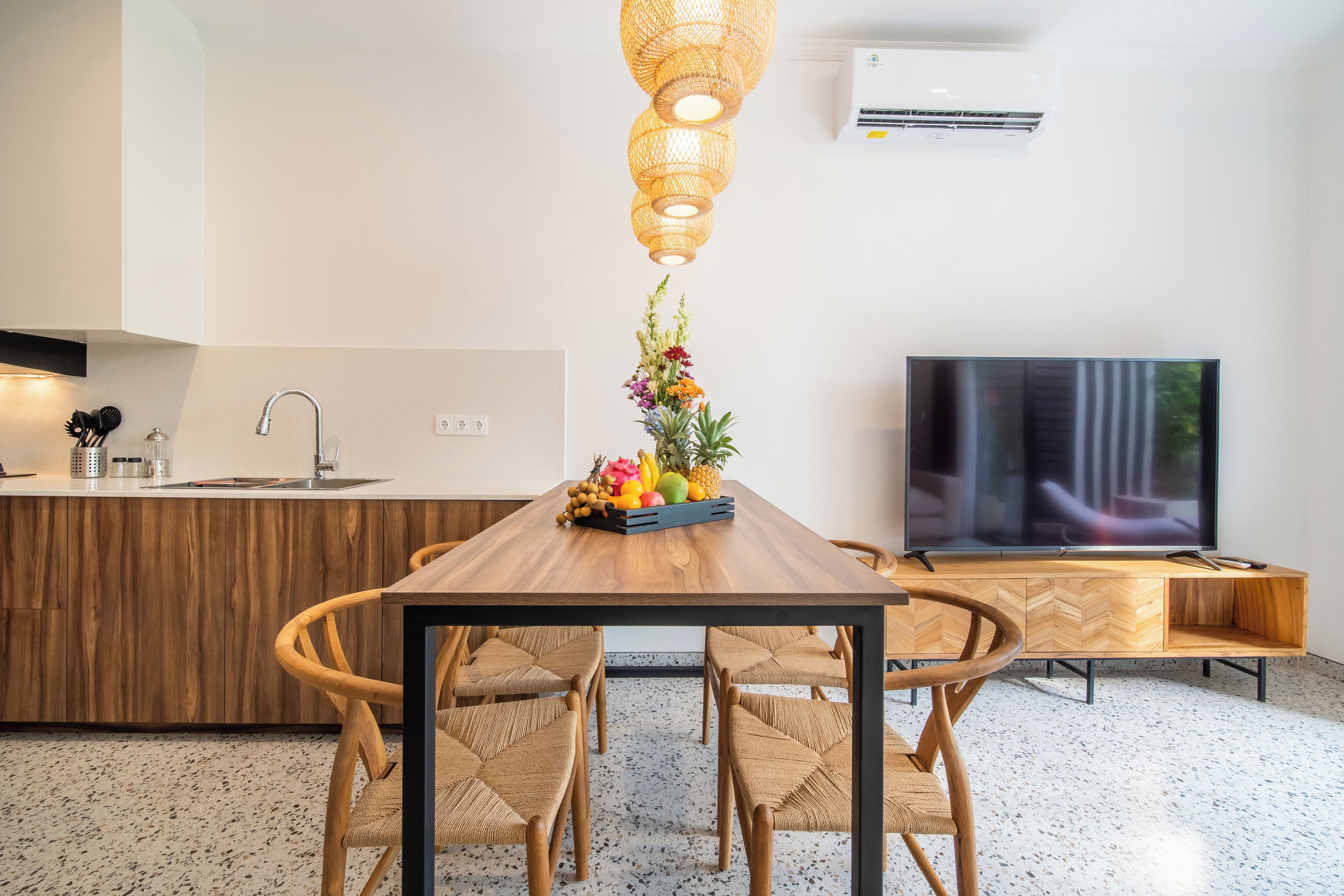 Una cocina moderna con una isla de madera, una mesa de comedor con sillas, un televisor y un accesorio de iluminación decorativo.