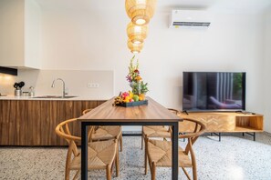 Una cocina moderna con una isla de madera, una mesa de comedor con sillas, un televisor y un accesorio de iluminación decorativo.