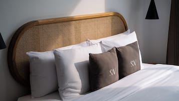 Una cama con ropa blanca, cabecera tejida y dos almohadas con un monograma.