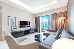 A modern living room with a sofa, a coffee table, a TV mounted on the wall, and a balcony with curtains. - Stylish 1BR Stay in DAMAC Paramount | Business Bay (Dubai)