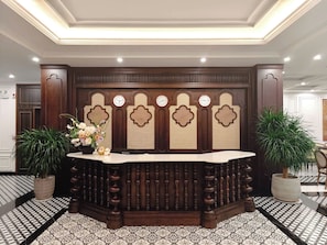 A reception desk with a clock, potted plants, and a patterned floor.