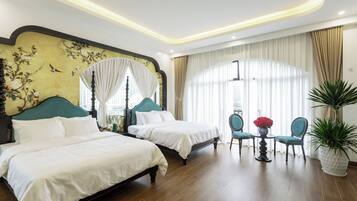 A hotel room with two beds, a sitting area with a table and chairs, and a large window with curtains.