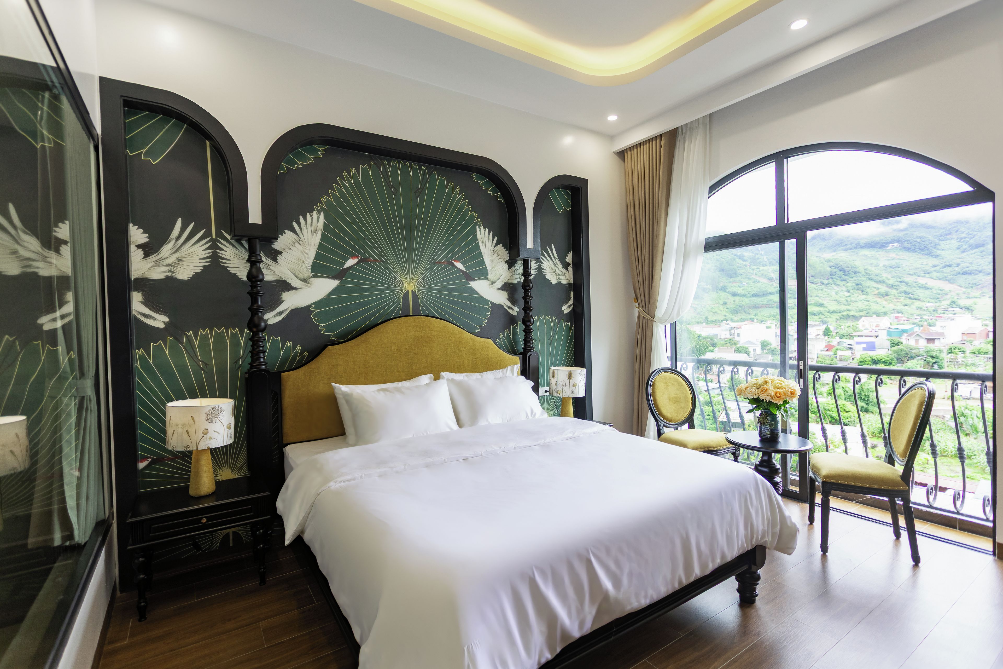 A hotel room with a large bed, a balcony with a view, and a decorative headboard.
