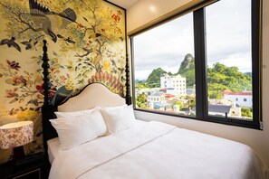 A bed with white linens, a headboard, and a window with a view of a cityscape and greenery.