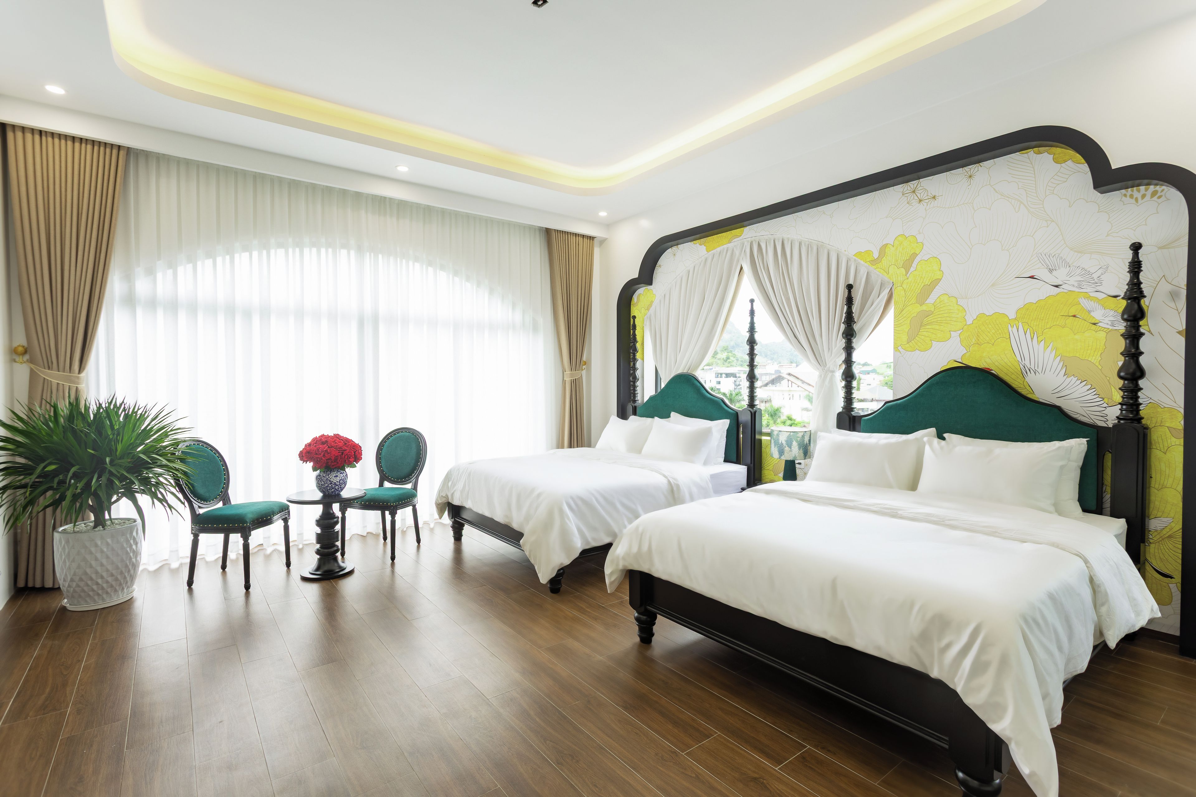 A hotel room with two beds, a sitting area with a table and chairs, and a large window with curtains.