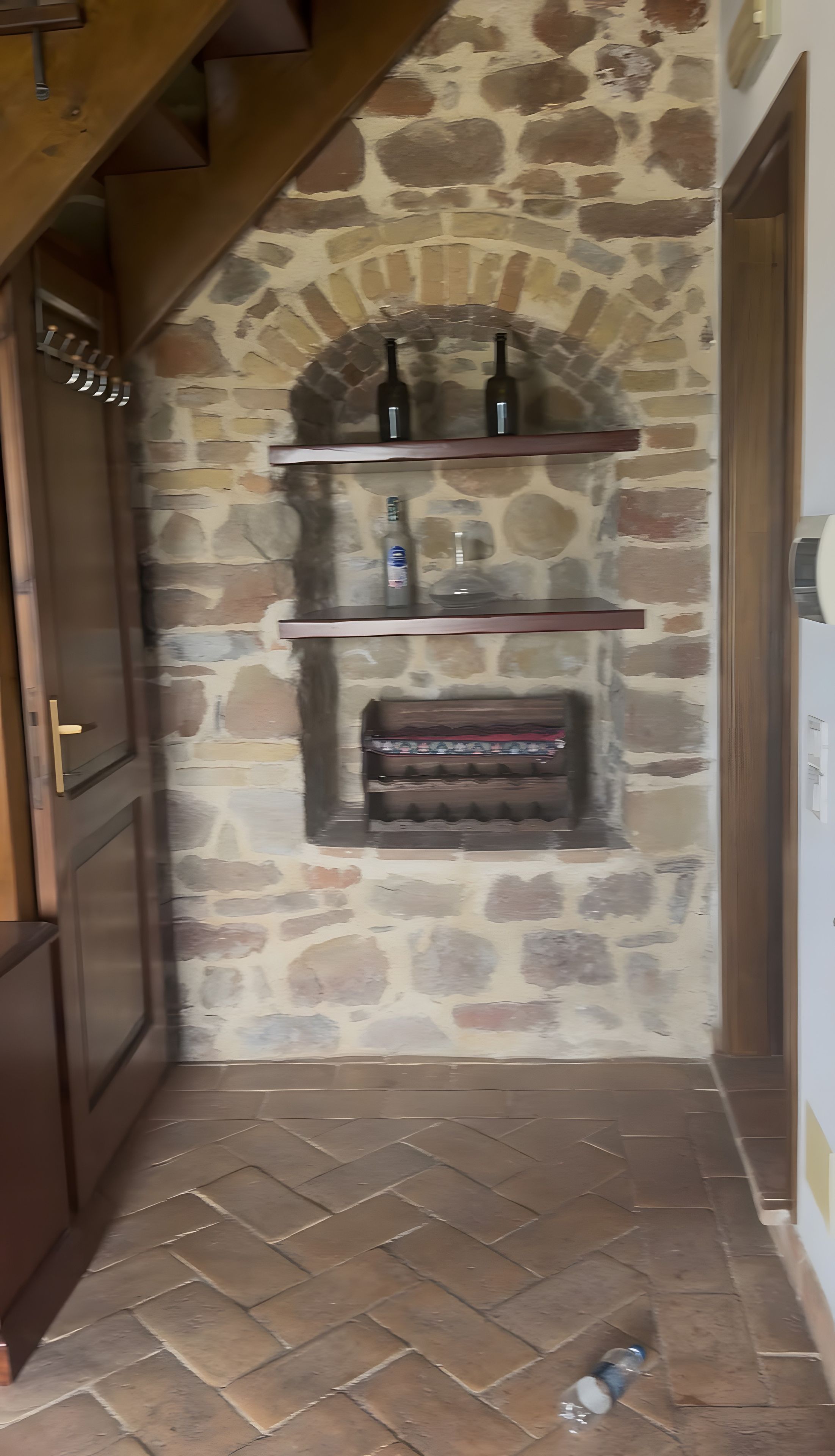 A stone fireplace with wine bottles and glasses, a wooden door, and a tiled floor.