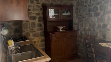Une cuisine avec un mur en pierre, des placards en bois, un évier et une chaise.
