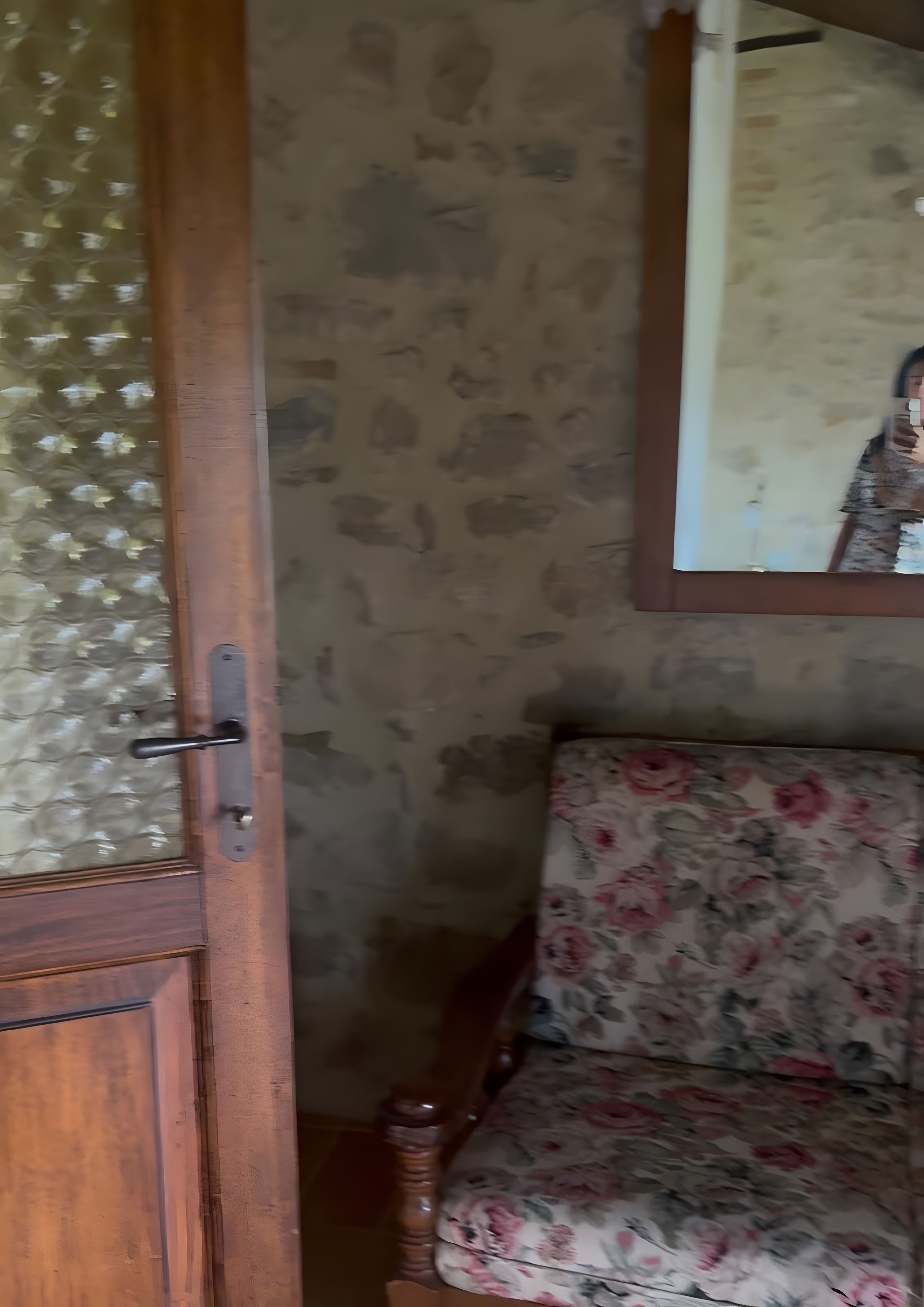 A room with a wooden door, a patterned wall, and a floral sofa.