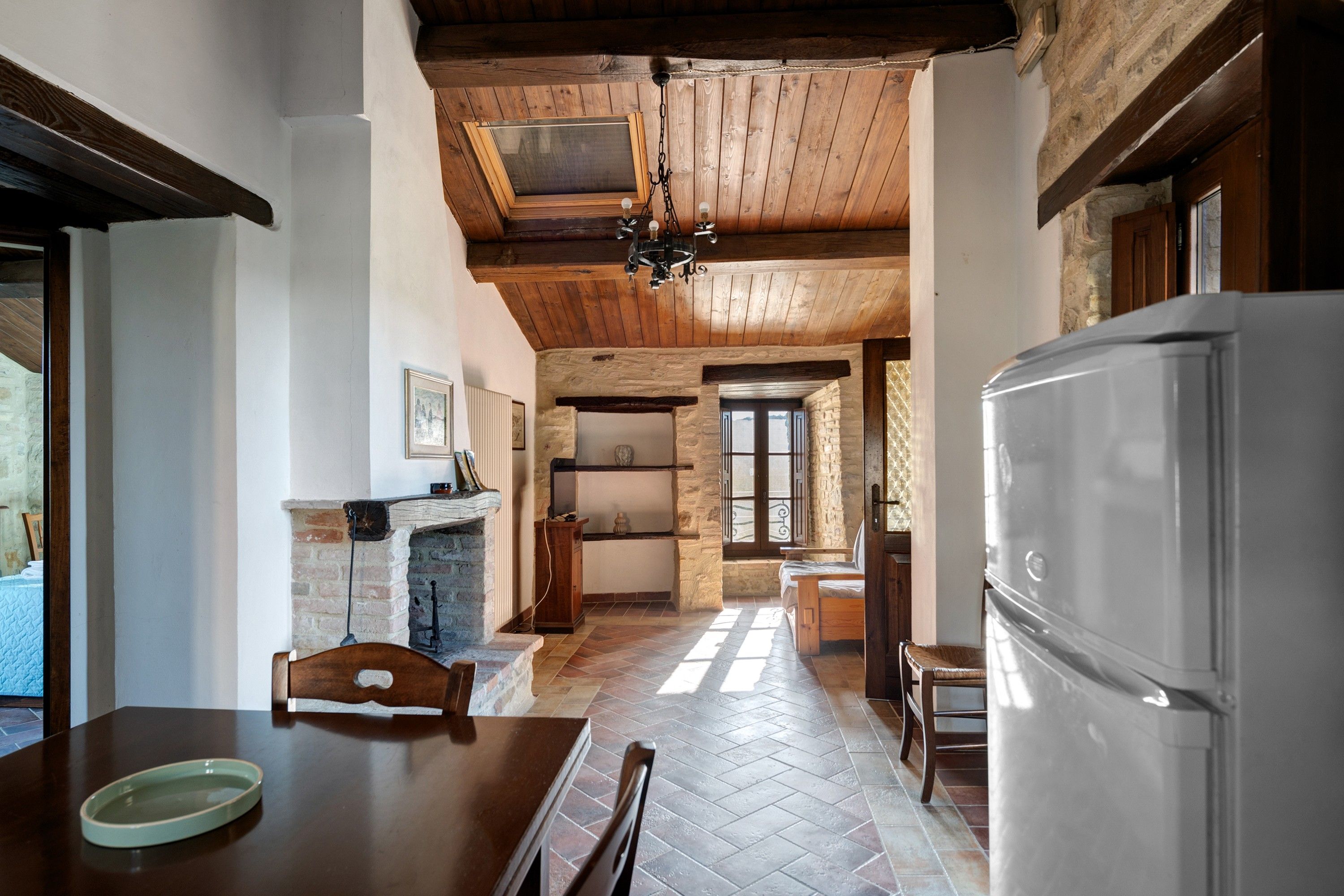 Eine rustikale Küche mit Kamin aus Stein, Holzbalken und einem großen Kühlschrank.