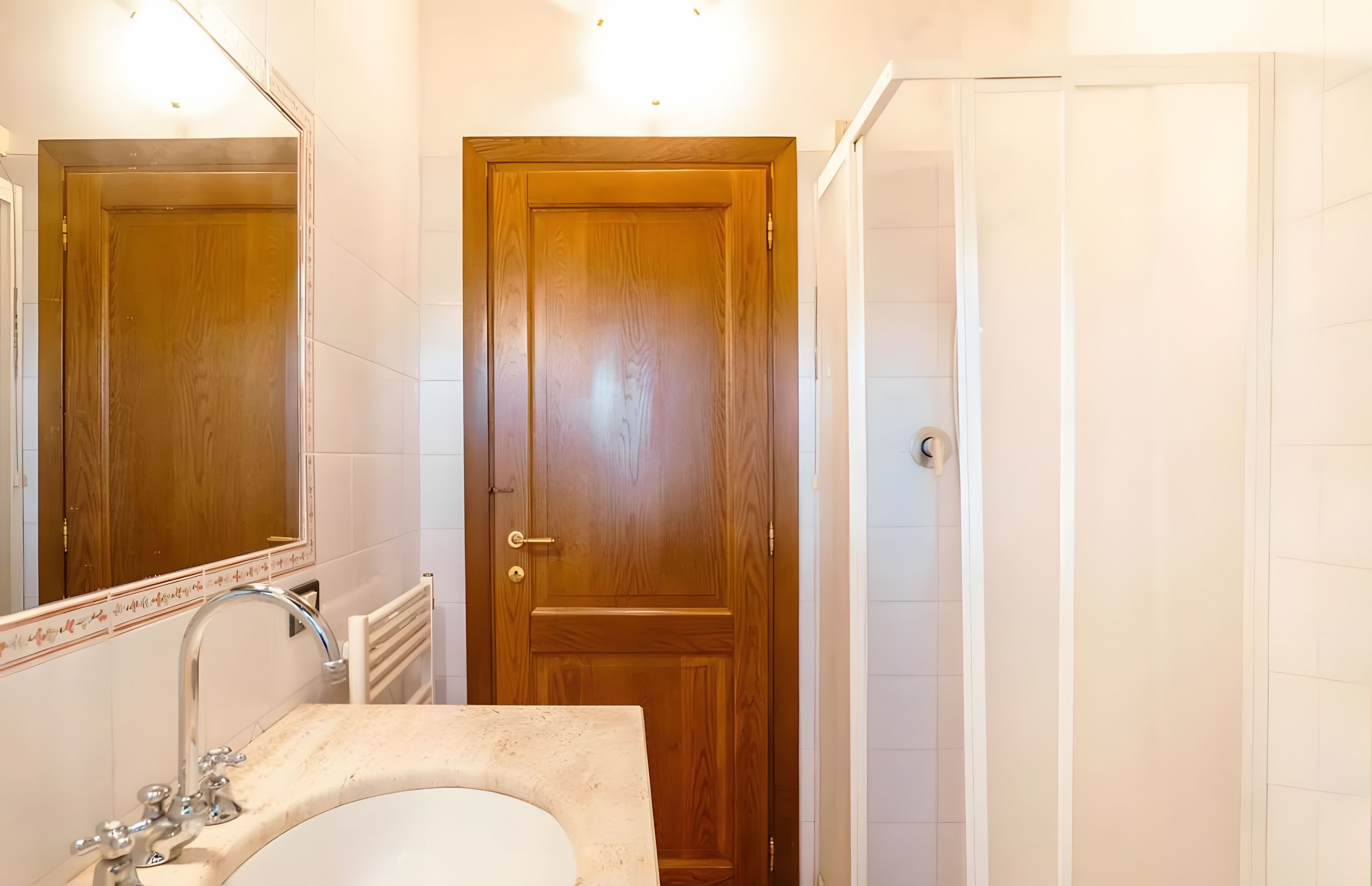 A bathroom with a wooden door, a sink with a mirror, and a shower area.