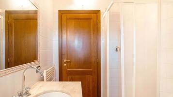 A bathroom with a wooden door, a sink with a mirror, and a shower area.