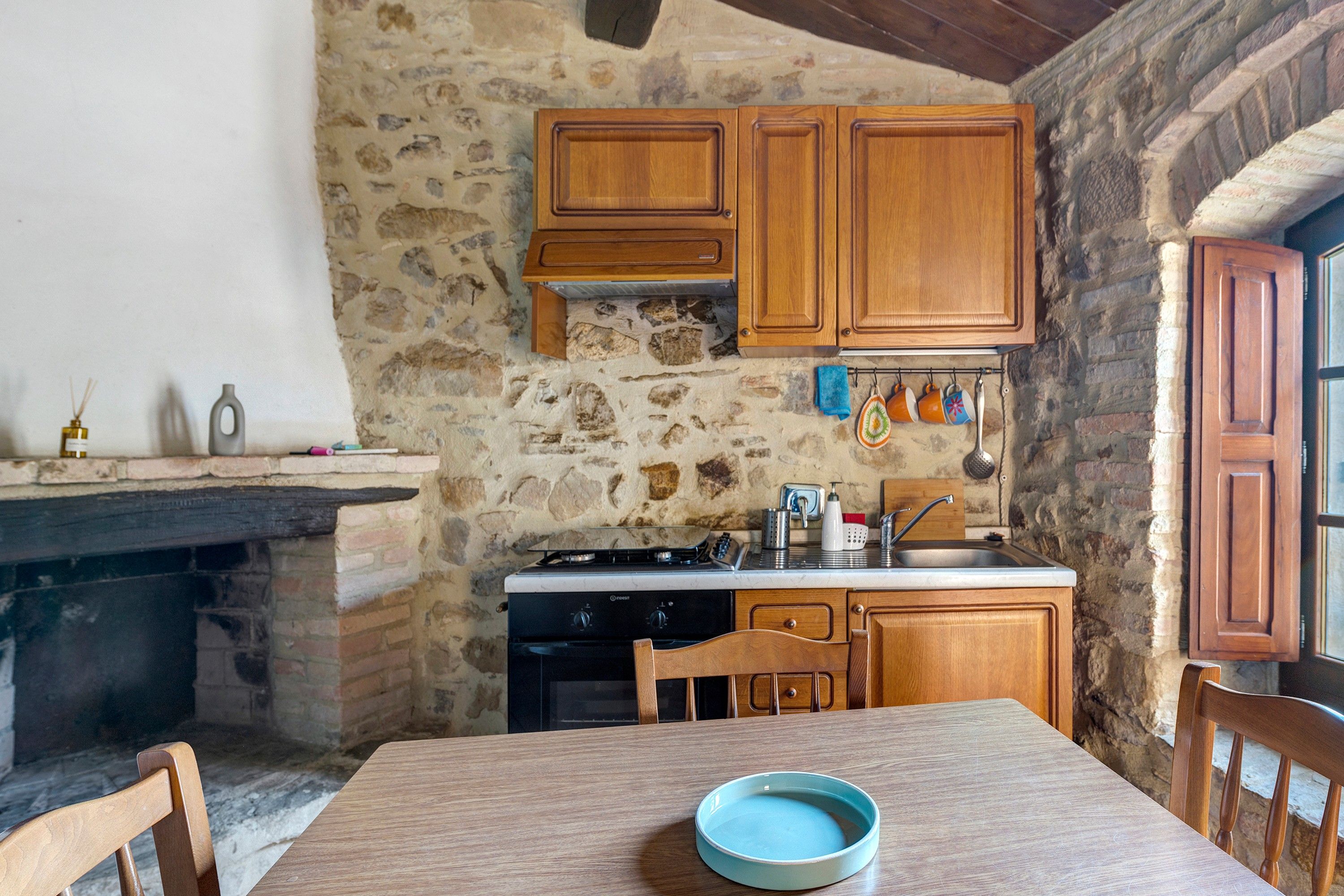 Una cocina rústica con armarios de madera, una pared de piedra y una mesa de comedor con sillas.