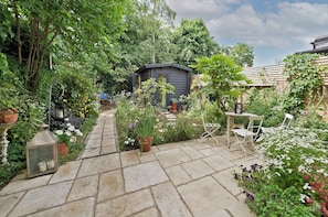 A garden with a stone pathway leading to a small shed, surrounded by various plants and flowers. - Kensal Rise Garden Oasis, by Veeve (London)
