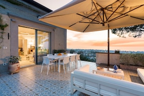 A terrace with a dining area, outdoor seating, and a view of the city at sunset. - Elegant villa with private pool and private hot tub in Capo d'Orlando - DiCasaInSicilia (Capo d´Orlando)