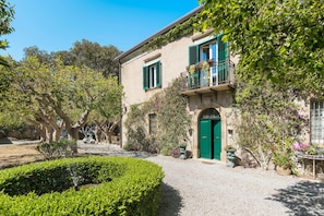 A building with a green door, a balcony with flowers, and a gravel driveway. - Elegant villa with private pool and private hot tub in Capo d'Orlando - DiCasaInSicilia (Capo d´Orlando)