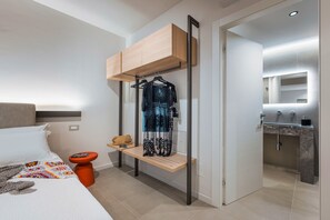 A modern hotel room with a bed, a bedside table, a hanging wardrobe, and a bathroom with a mirror and sink. - Luxurious villa with outdoor pool, heated indoor pool, wellness area, and outdoor Jacuzzi in Cornino – DiCasaInSicilia (Custonaci)