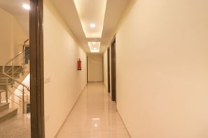 A hallway with a staircase on the left, a fire extinguisher on the wall, and a door on the right. - Hotel O Comfort Residency  (Gurugram)