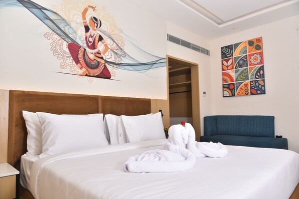 Quarto de hotel com uma cama grande, um sofá azul, uma parede com uma pintura abstrata colorida e um mural decorativo.
