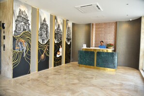 Un espace d’accueil doté d’un sol en marbre, d’un comptoir de réception et d’un mur orné d’une fresque représentant l’architecture d’un temple.