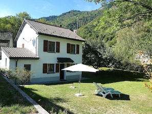 A two-story house with a tiled roof, a white exterior, and a small front yard with a lawn and a white umbrella. - Wonderful private villa for 4 guests with WIFI, TV and patio (Scona)