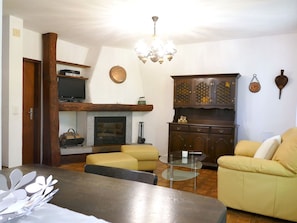 Ein Wohnzimmer mit Kamin, Fernseher, einer Chandelierleuchtre, einem Schrank und einem Sofa.