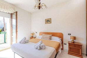 Une chambre d’hôtel avec un lit, deux tables de chevet, un lustre, une fenêtre avec des stores et un tableau au mur.
