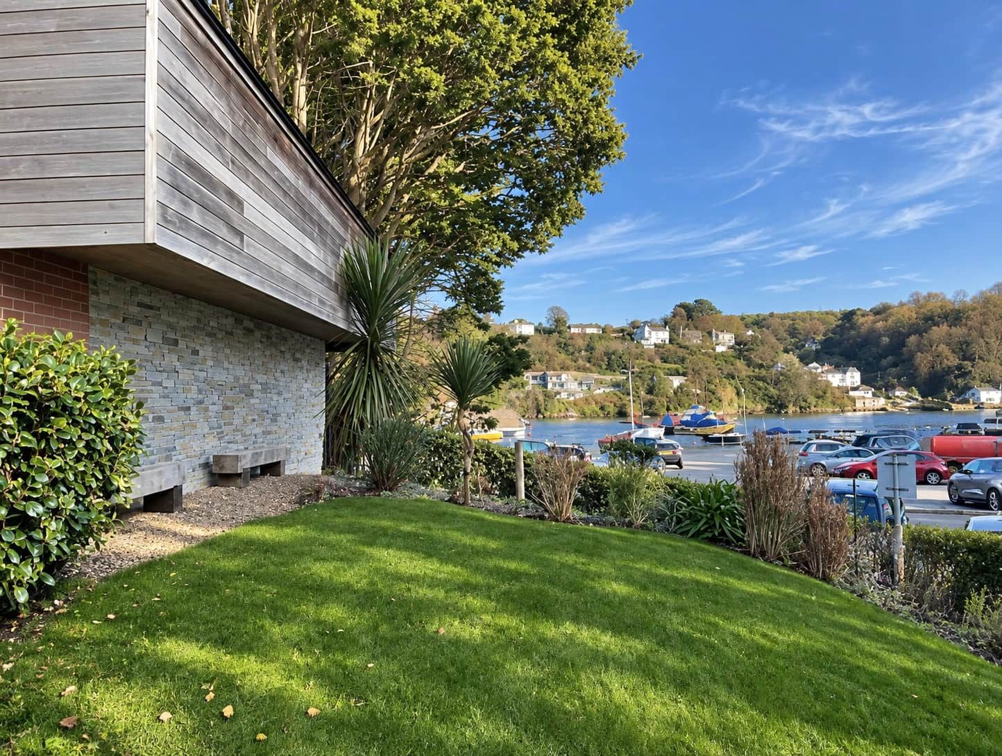 A building with a stone facade, a grassy lawn, and a parking lot with cars.