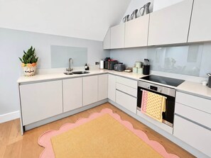Eine moderne Küche mit weißen Schränken, einer Spüle, einem Herd und einer Arbeitsplatte mit verschiedenen Küchenutensilien.