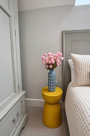 Ein Badezimmer mit Toilette, einem Nachttisch mit Blumenvase und einem Bett mit gemustertem Bettbezug.