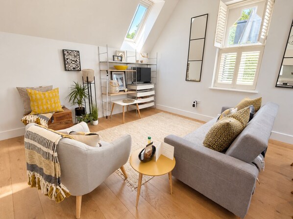 Ein modernes Wohnzimmer mit einer offenen Decke, einem grauen Sofa, einem Couchtisch und einem Fernseher auf einem Schrank.