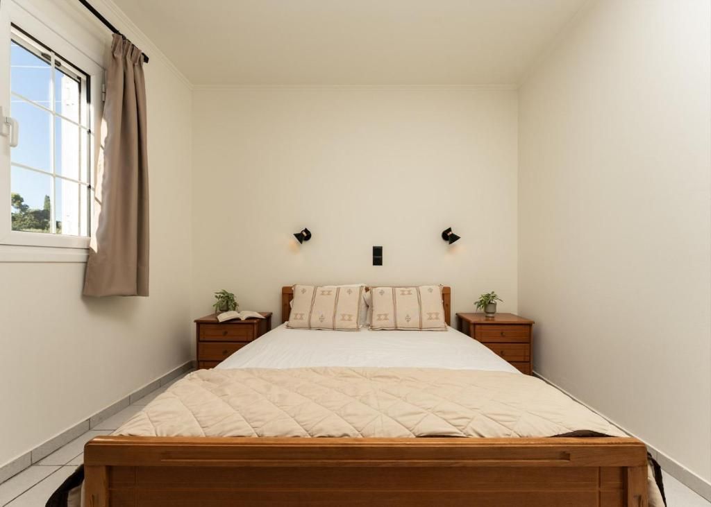 Un dormitorio con cama de madera, dos mesitas de noche, una ventana con cortinas y una lámpara fijada a la pared.