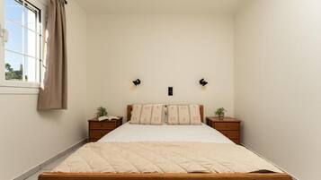 Un dormitorio con cama de madera, dos mesitas de noche, una ventana con cortinas y una lámpara fijada a la pared.