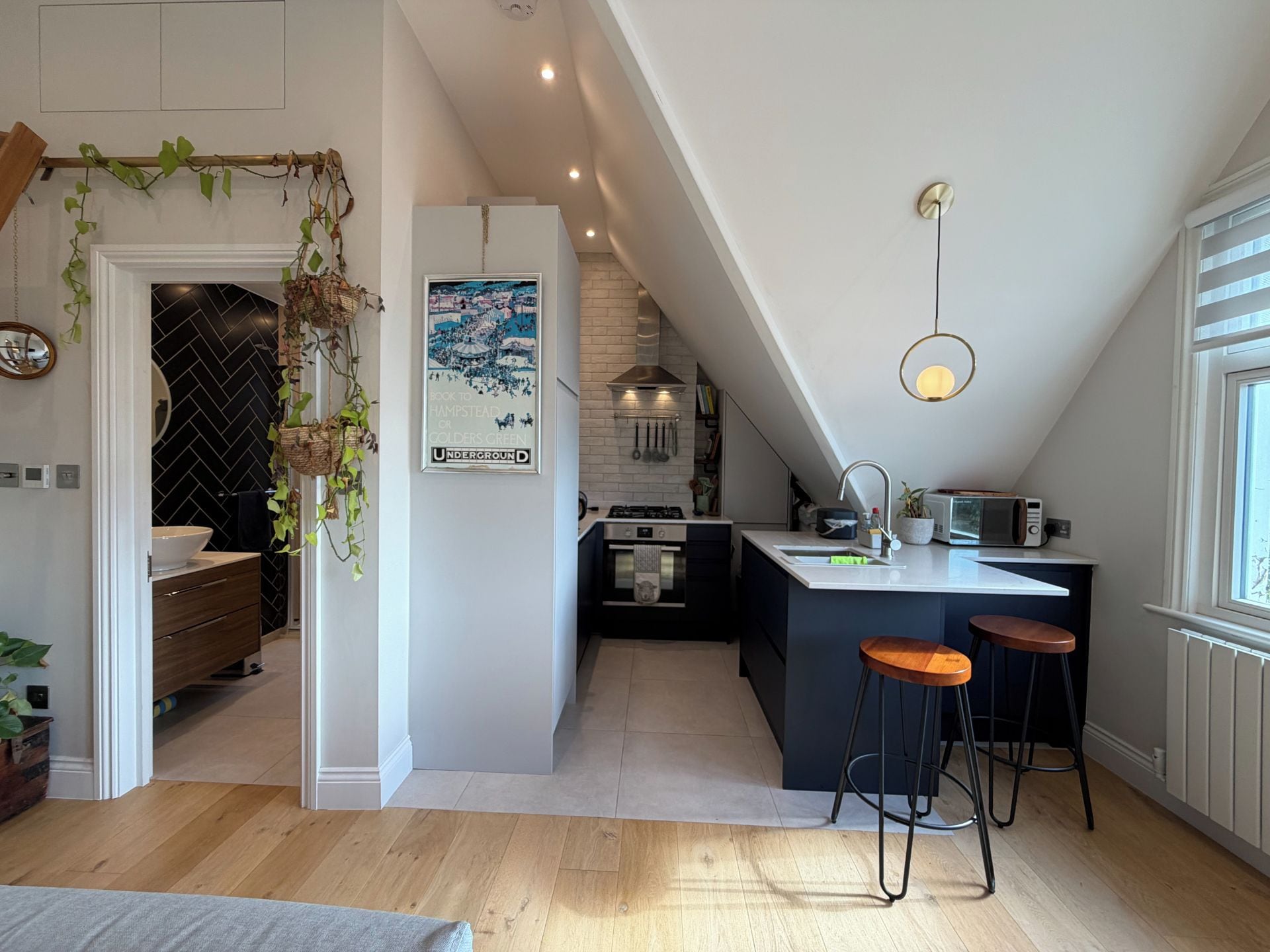 A modern kitchen with a central island, bar stools, and a hanging plant.