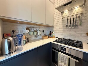 Una cucina moderna con piano cottura a gas, bollitore e diversi utensili appesi al muro.