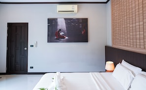 Ein Hotelzimmer mit einem Bett, einer Wand-Klimaanlage, einem Gemälde, einer Tür und einem Nachttisch mit Lampe.