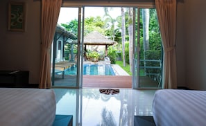 Ein Hotelzimmer mit Glastür zum Poolbereich, einem strohgedeckten Gebäude und Blick auf üppiges Grün.