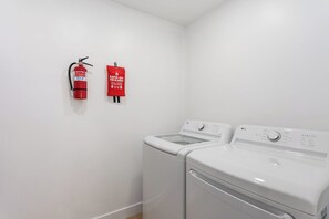 A laundry room with two white washing machines and a red fire extinguisher mounted on the wall. - This house is a 3 bedroom(s), 2 bathrooms, located in Tempe, AZ. (Tempe)