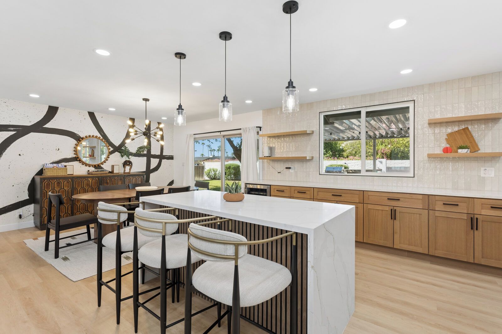 A modern kitchen with a central island, bar stools, pendant lighting, and a large window.