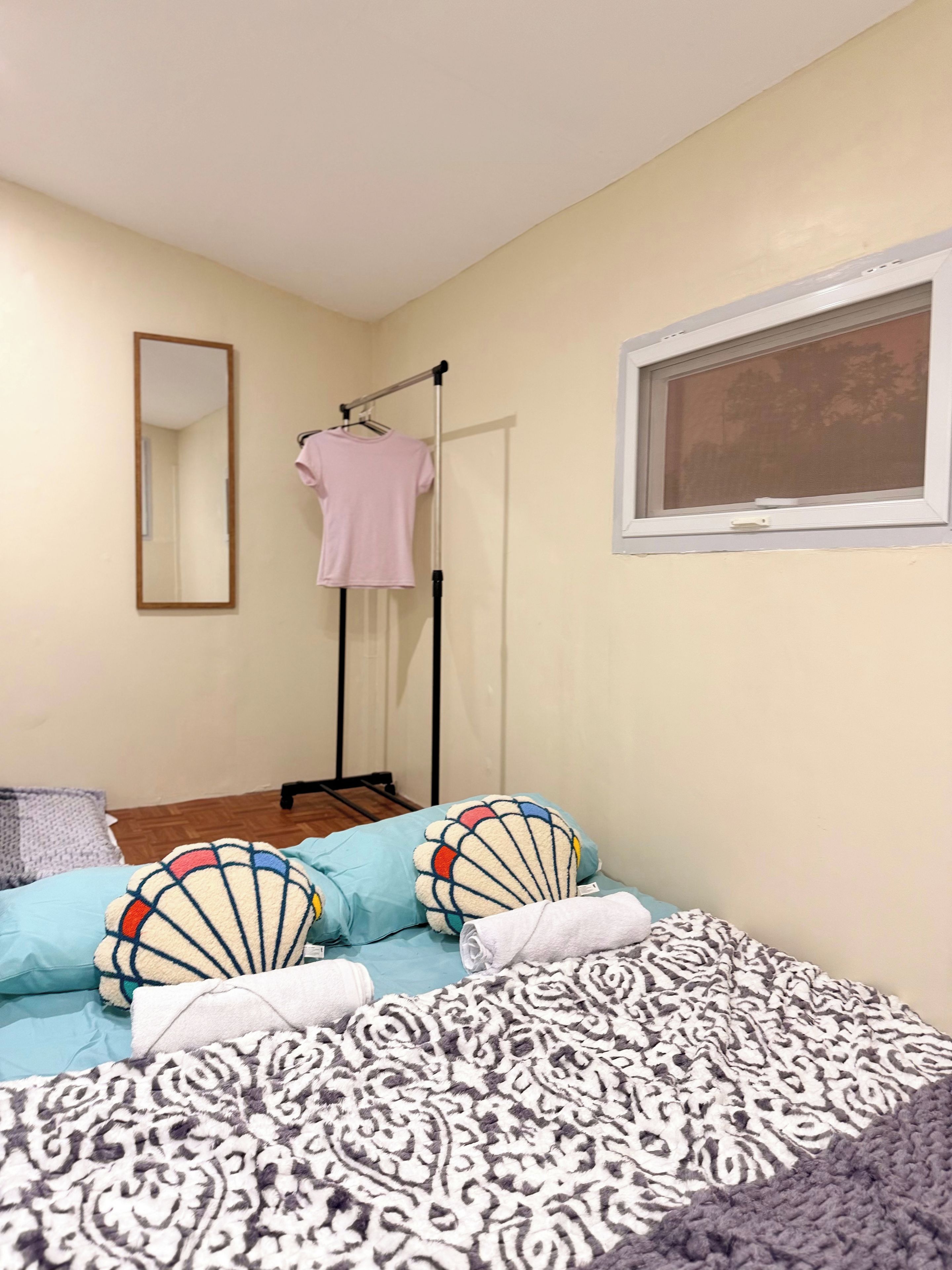 A bedroom with a bed, pillows, a hanging clothes rack, a window, and a mirror.