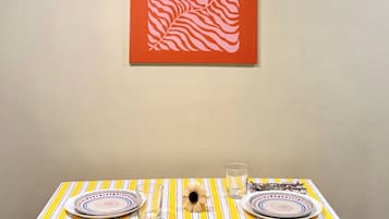 Mesa de jantar com toalha listrada, pratos, talheres e um copo. Uma obra de arte emoldurada está na parede acima.