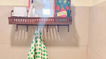 A bathroom with a shelf holding toiletries, a polka-dotted towel, a toilet with a decorative hand-shaped soap holder, and a shower.
