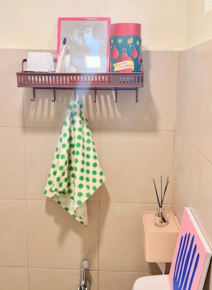 Et badeværelse med en hylde med toiletartikler, et stribet håndklæde, et toilet med en dekorativ sæbeholder formet som en hånd, og en bruser.