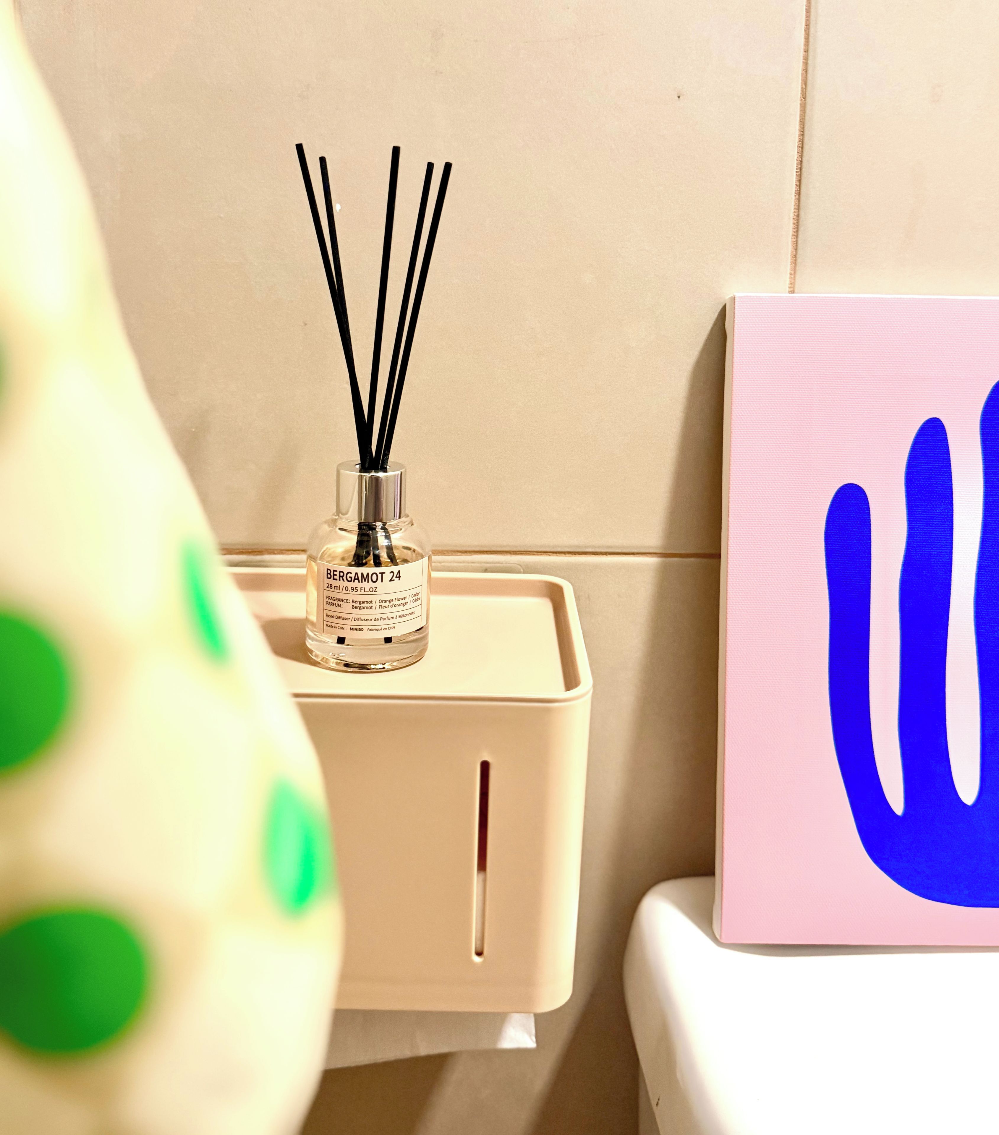 Quarto com parede bege, armário branco com um frasco de Bergamot 24 e uma caixa rosa com desenho azul.