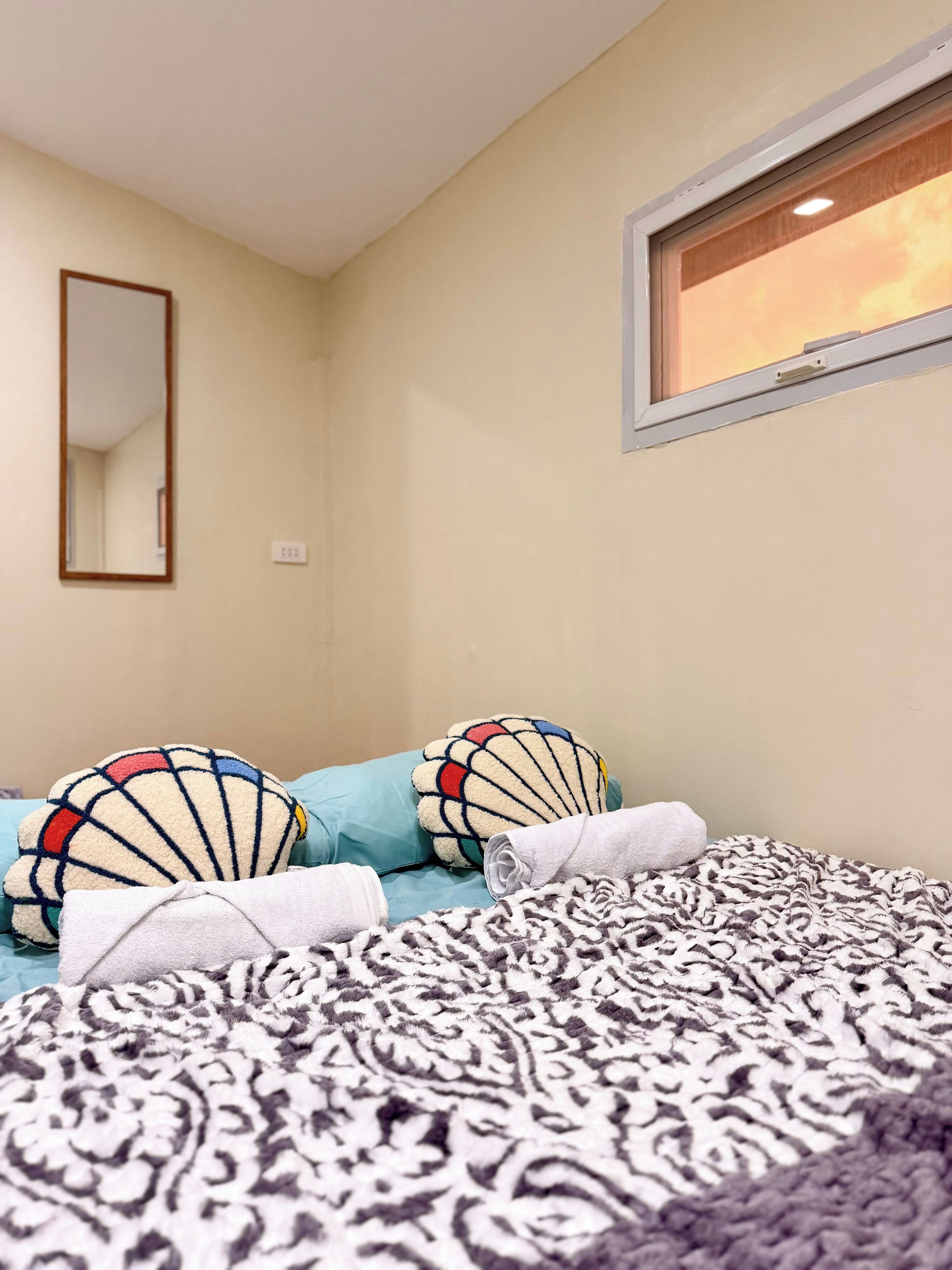 A bedroom with a bed, pillows, a window, and a mirror.