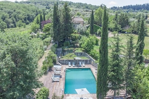 A large rectangular pool with a wooden deck, surrounded by tall trees and a stone wall. - Villa Grevigiana 12 pool and SPA - My Rental Homes (Panzano In Chianti)