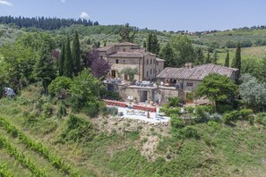 A stone building with a terrace and outdoor seating area surrounded by greenery. - Villa Grevigiana 12 pool and SPA - My Rental Homes (Panzano In Chianti)