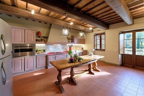 A spacious kitchen with a wooden table, modern appliances, and a view of the outdoors. - Villa la Rondine pool and spa - My Rental Homes (Torricella)
