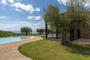A swimming pool with a curved edge, surrounded by a paved area and grass. - Villa la Rondine pool and spa - My Rental Homes (Torricella)