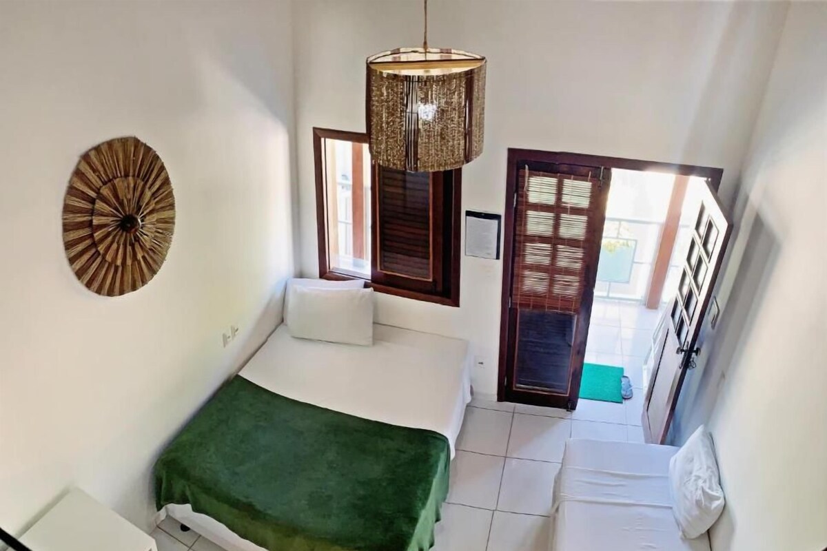 Een slaapkamer met een bed, een groene plaid, een hanglamp en uitzicht op buiten.